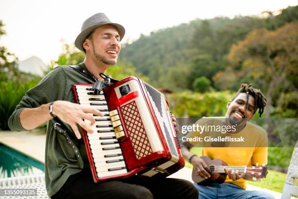 zwei verschiedene junge musiker, die draußen mit verschiedenen instrumenten jammen - ukulele stock-fotos und bilder