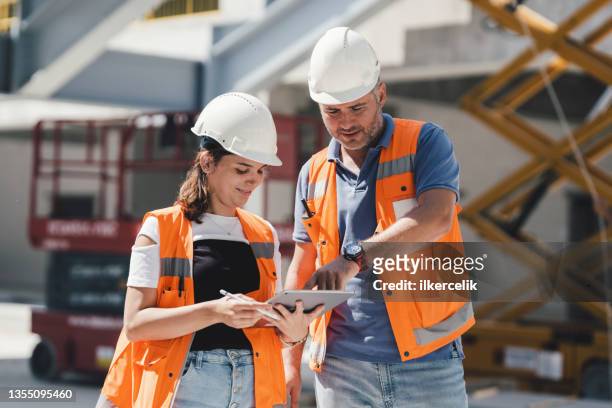 civil engineers checking works according to project using digital tablet at construction site - bouwvakker stockfoto's en -beelden