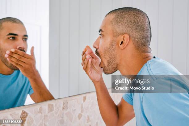 shot of a young man smelling his breath during his morning grooming routine at home - bad breath stock pictures, royalty-free photos & images