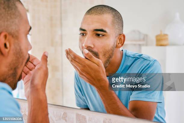 shot of a young man smelling his breath during his morning grooming routine at home - zichtbare adem stockfoto's en -beelden
