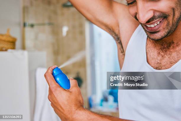 shot of a young man spraying deodorant on his armpit in the bathroom at home - man spraying stock pictures, royalty-free photos & images