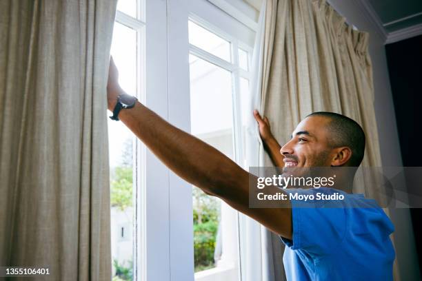 shot of a young man opening up the curtains in a bedroom at home - curtain imagens e fotografias de stock