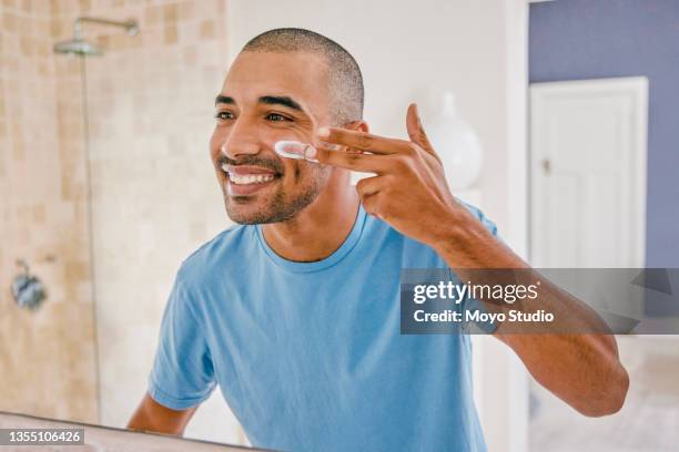 shot of a young man applying moisturizer to his face in the bathroom at home - applying imagens e fotografias de stock