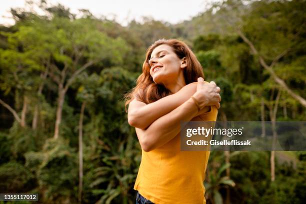 mujer sonriente dándose un abrazo afuera en verano - abrazo fotografías e imágenes de stock