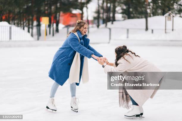 two happy positive teenage girls friends in warm fur coats are having fun walking skating on a skating rink in the winter forest during the christmas vacation. a couple of women in love spend time together in nature in cold winter - isrink bildbanksfoton och bilder