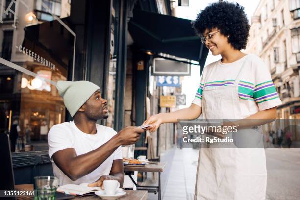 african american tourist in madrid paying for his coffee at the sidewalk cafe - madrid shopping stock pictures, royalty-free photos & images