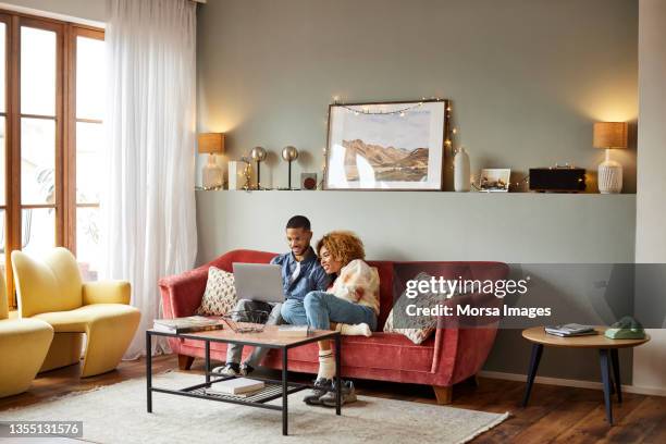 couple with laptop on sofa in living room at home - young man laptop couch photos et images de collection