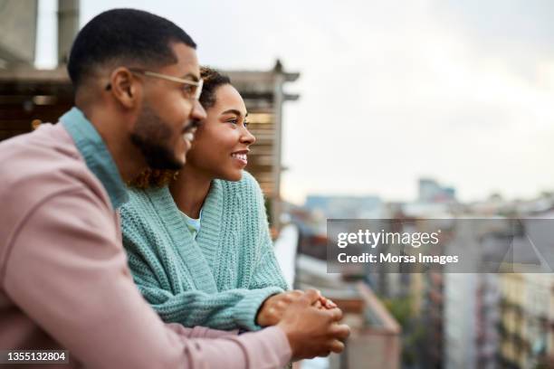 couple looking away while holding hands at rooftop - young couple happy stock pictures, royalty-free photos & images