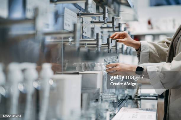 young asian woman shopping in a package-free refill store, refilling body wash into a glass bottle. shopping for fair trade and organic personal care products. zero waste, plastic free, ecologically friendly, green living and sustainable lifestyle - ricaricare foto e immagini stock