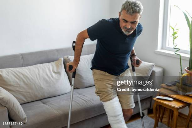 hombre con la pierna rota tratando de levantarse del sofá - crutches fotografías e imágenes de stock