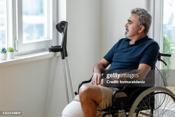 man in wheelchair in front of window - accident recovery stockfoto's en -beelden