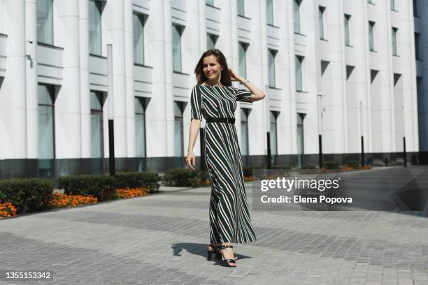 young elegant woman in striped maxi dress walking at the city - gestreiftes kleid stock-fotos und bilder