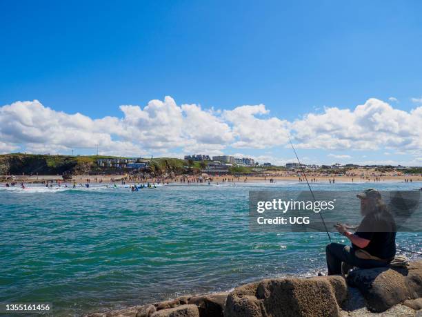 Man fishing off the rocks on the breakwater, Bude, Cornwall, UK.