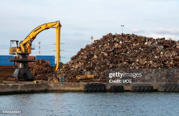 Southampton, England, UK, A yellow crawler excavator machine on a dockside moving scrap metal before loading onto a cargo ship for exporting.