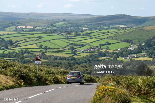 Dartmoor, Devon, England, UK, A small car travelling with a high view over Dartmoor near Widecombe on the Moor with backdrop of green fields and...