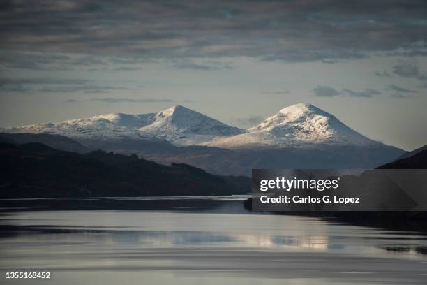 snowy mountains under a dramatic cloudy sky in perth and kinross, highlands of scotland, united kingdom, with the snow-capped range reflected on the waters of the loch tay - perth scotland 個照片及圖片檔