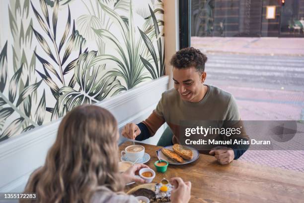 romantic multiracial couple eating fresh croissants with coffee, having breakfast in coffee shop - felicidad duran fotografías e imágenes de stock