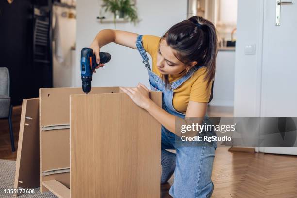 skilled girl using electric screwdriver to fold a wooden shelf - electric screwdriver stock pictures, royalty-free photos & images