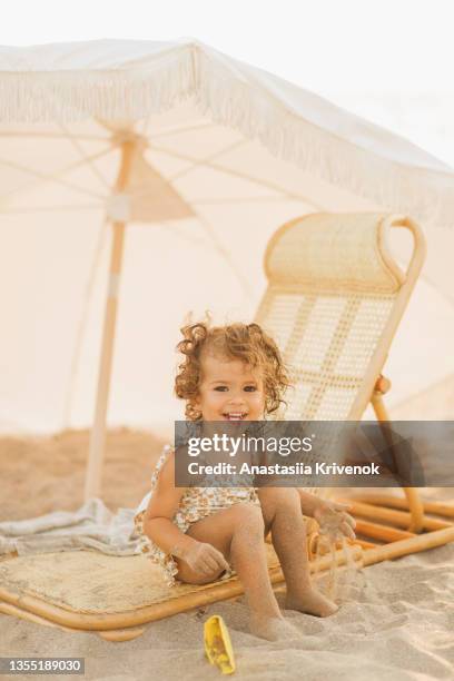 little cute baby girl is playing on a beach near a sea. - sombrilla playa fotografías e imágenes de stock