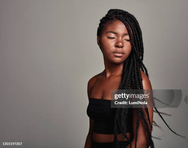 studio shot of an attractive young woman tossing her hair against a grey background - braids stock pictures, royalty-free photos & images