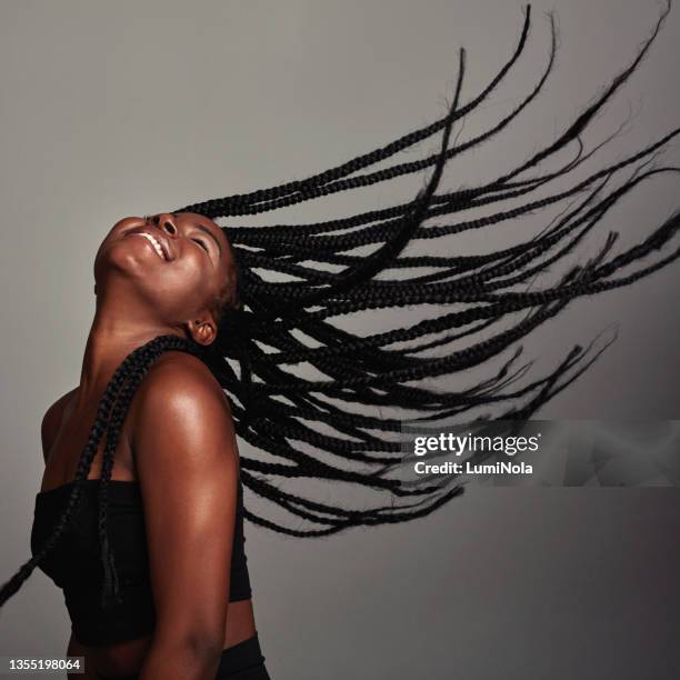 studio shot of an attractive young woman tossing her hair against a grey background - beautiful braid stockfoto's en -beelden