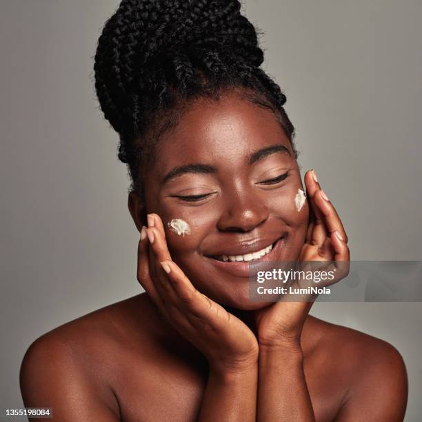 foto de estudio de una atractiva joven que se aplica crema hidratante sobre un fondo gris - applying fotografías e imágenes de stock