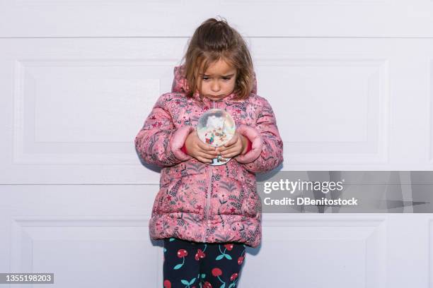 little girl wearing pink coat and hood, holding a glass christmas snow globe on white background. christmas, decorations, celebration and winter concept. - madrid snow stock pictures, royalty-free photos & images