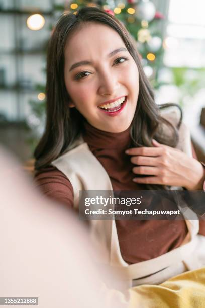 cheerful attractive asian female woman video calling to her friend invite all to christmas party at apartment,pov video calling of asian female with christmas decorating tree in living room at home talking invite her family distance relation - stay at home saying stock pictures, royalty-free photos & images