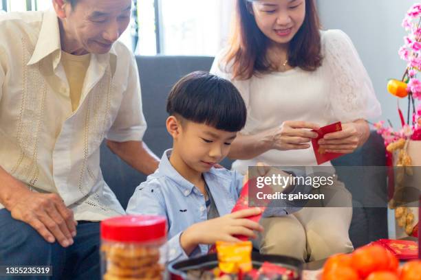 asian boy helping mother and grandfather to prepare red envelops (lai see) at home for chinese new year - kids making money stock pictures, royalty-free photos & images