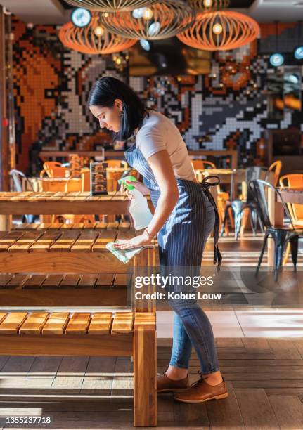 shot of a young woman disinfecting the tables while working in a restaurant - restaurant cleaning stock pictures, royalty-free photos & images