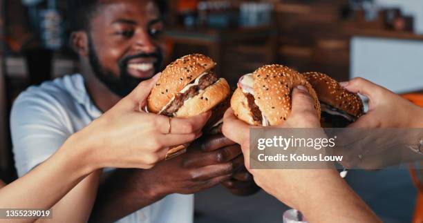 scatto di un gruppo di giovani amici che gustano deliziosi hamburger in una tavola calda - hamburger foto e immagini stock