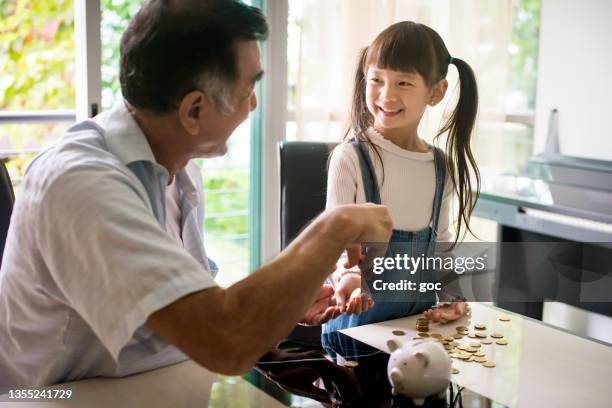 asiatischer großvater, der seiner enkelin beibringt, geld im sparschwein zu sparen - save money stock-fotos und bilder
