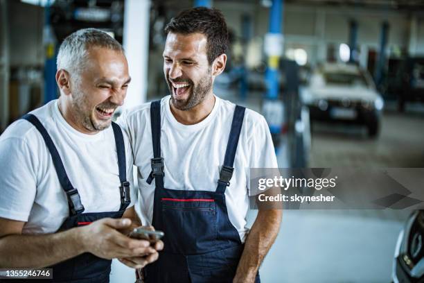 cheerful auto mechanics using cell phone in a workshop. - laughing fun bildbanksfoton och bilder