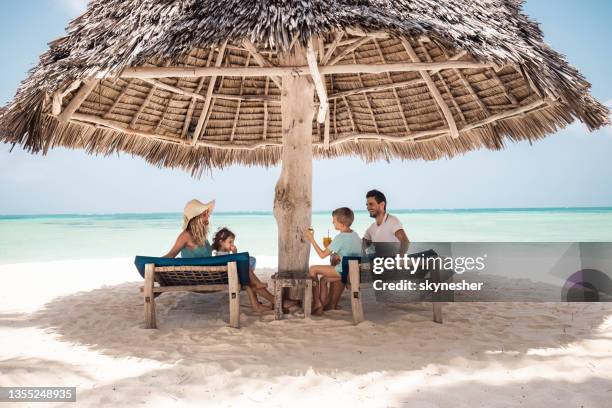 familia feliz hablando bajo sombrilla en la playa. - sombrilla playa fotografías e imágenes de stock