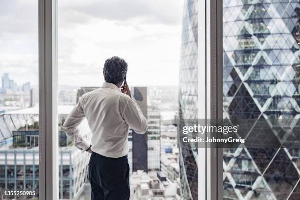 british executive talking on smart phone in office with view - grey hair back stock pictures, royalty-free photos & images