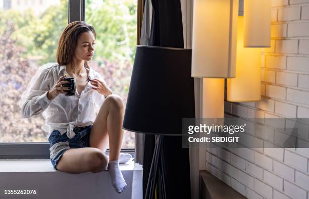young woman sitting on window and relaxing - human trafficking stock pictures, royalty-free photos & images