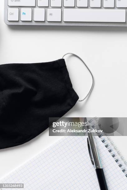 compliance with safety and hygiene measures in the office. preventing the spread of the covid-19 coronavirus epidemic. a protective face mask, a keyboard from a computer or laptop, a pen with a notepad, on a freelancer's desktop or a white background. - siberian mouse fotografías e imágenes de stock