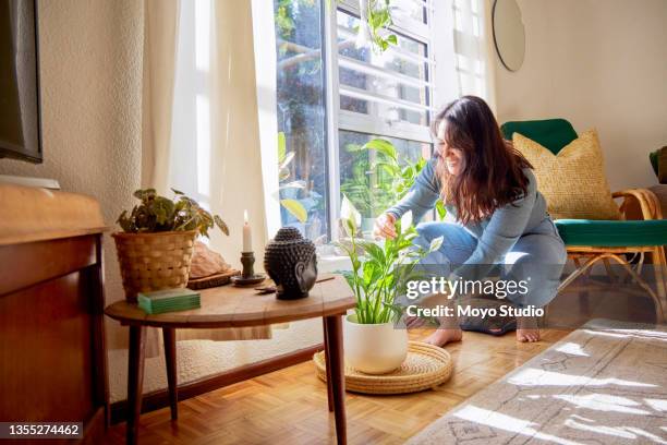 full length shot of an attractive young woman rearranging her living room at home - neat stock pictures, royalty-free photos & images