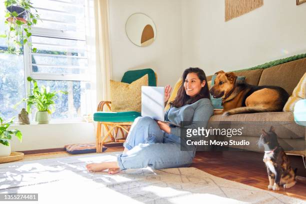 tiro completo de uma jovem atraente sentado em sua sala de estar com seus animais de estimação e usando seu laptop - dog and cat - fotografias e filmes do acervo