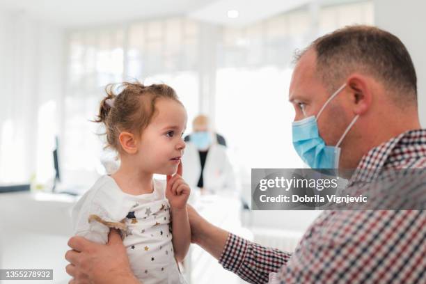 man with protective mask consoling his daughter at doctor's office - receiving treatment concerned stock pictures, royalty-free photos & images