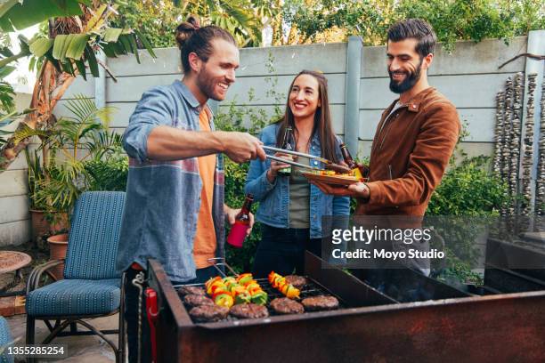 shot of a young man serving up grilled food to his friend - barbecue bildbanksfoton och bilder