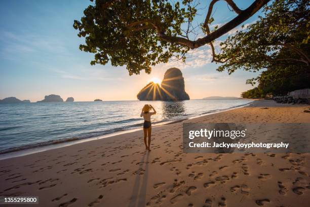 a young woman standing and looking on the rock in railay east beach in the golden twilight time moment, krabi province, thailand - krabi stock pictures, royalty-free photos & images