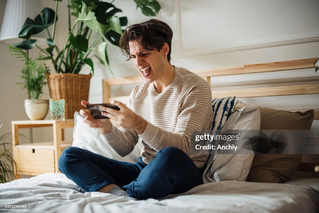 Junger Mann, der Videospiele auf seinem Smartphone spielt und wütend wird, als er das Spiel verliert