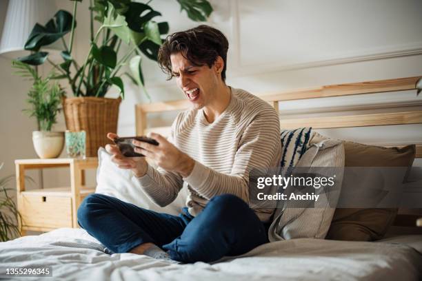 young man playing video games on his smartphone and gets angry as he lose the game - gaming mobile stock pictures, royalty-free photos & images