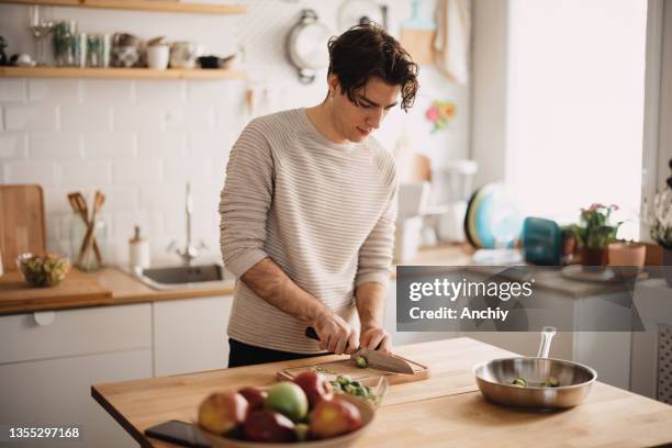junger mann bereitet in der küche das mittagessen zu, schneidet rosenkohl in winzige stücke - mann kocht stock-fotos und bilder