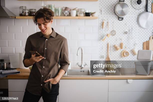 jeune homme souriant et parlant au téléphone dans la cuisine - brasses photos et images de collection