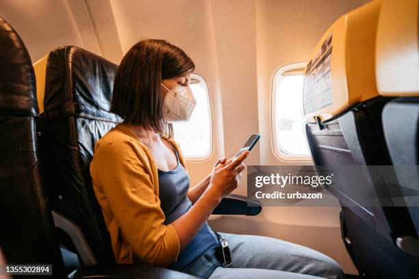 mujer con mascarilla está usando teléfono inteligente en avión - n95 face mask fotografías e imágenes de stock