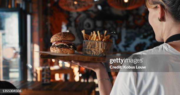 aufnahme einer kellnerin, die in einem restaurant einen burger mit pommes frites serviert - kellner oder kellnerin stock-fotos und bilder