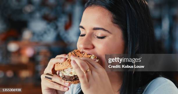 shot of a young woman enjoying a delicious burger at a restaurant - eating burger stock pictures, royalty-free photos & images