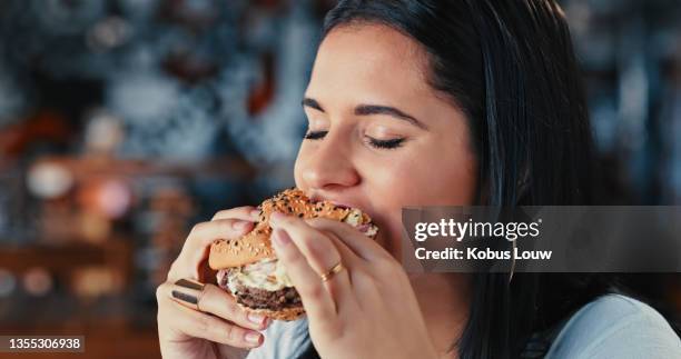 shot of a young woman enjoying a delicious burger at a restaurant - craving food stock pictures, royalty-free photos & images